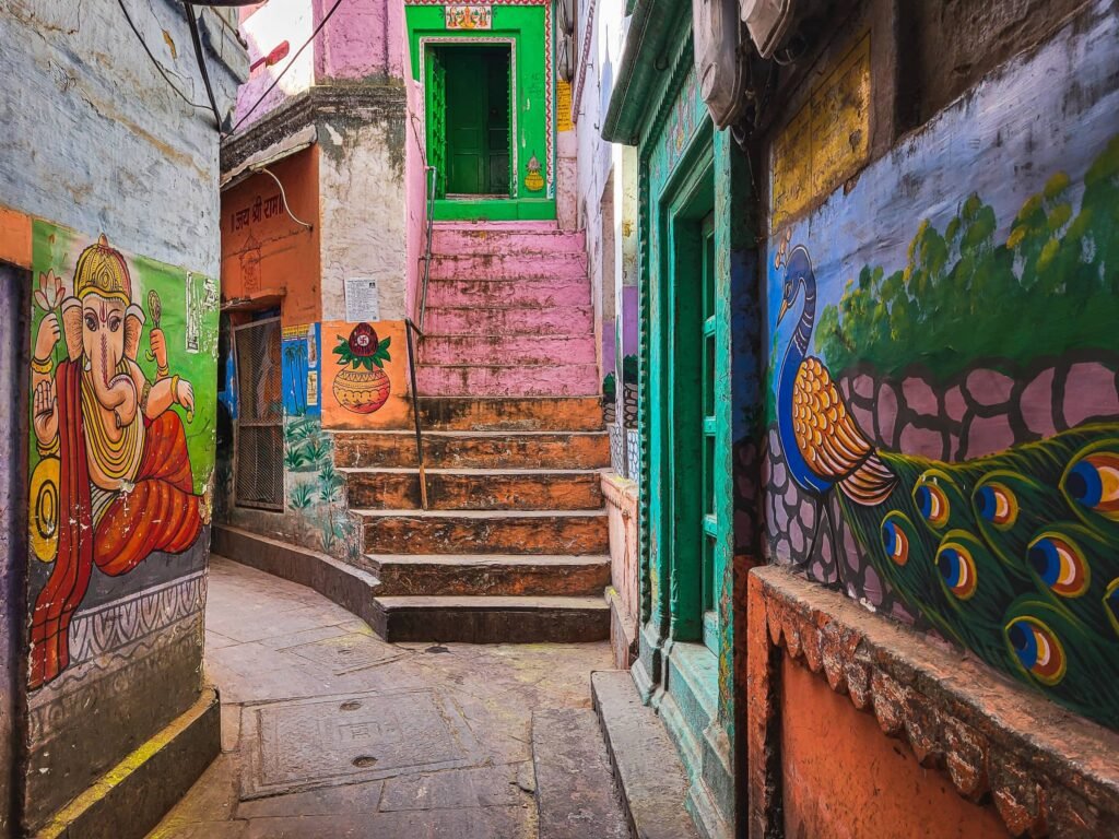 A narrow, brightly painted lane with Ganesha and peacock murals and coloured steps in the old city of Varanasi